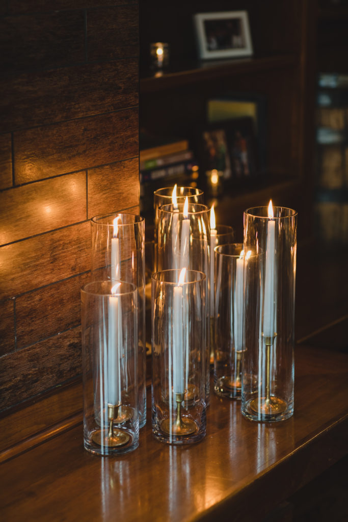Cozy and elegant gathering of grey taper candles with brass candle sticks in hurricane candleholders for a wedding at Revolution Brewing Chicago. 