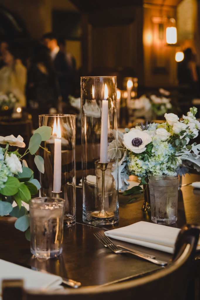 Revolution Brewing wedding ceremony arrangements in brass vases with anemones, blue hydrangea, spray roses, stock, and dusty miller; Grey taper candles with brass base in hurricane candleholders.