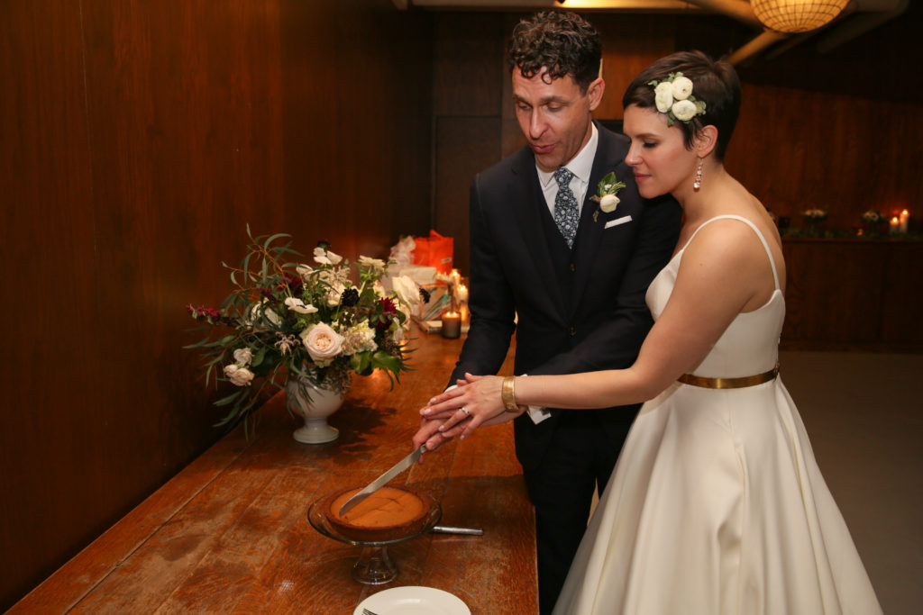 Bride and groom cutting pie for a fall wedding at Artifact Events in Chicago; bride wears white ranunculus flower hair accessory.