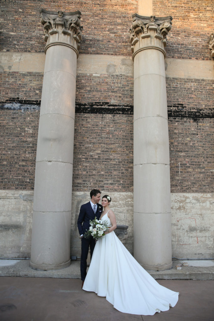 Formal wedding portrait with bride and groom, stone column background, and a monochromatic bouquet of garden roses, anemone, berries, lisianthus, and eucalyptus for  a beautiful wedding in Chicago. 