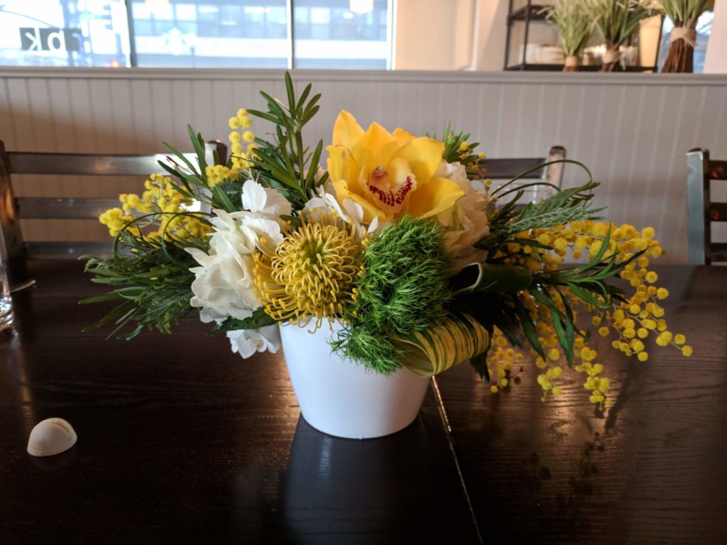 Yellow, white and green fwinter loral centerpiece with pincushion protea, cymbidium orchids, and acacia.
