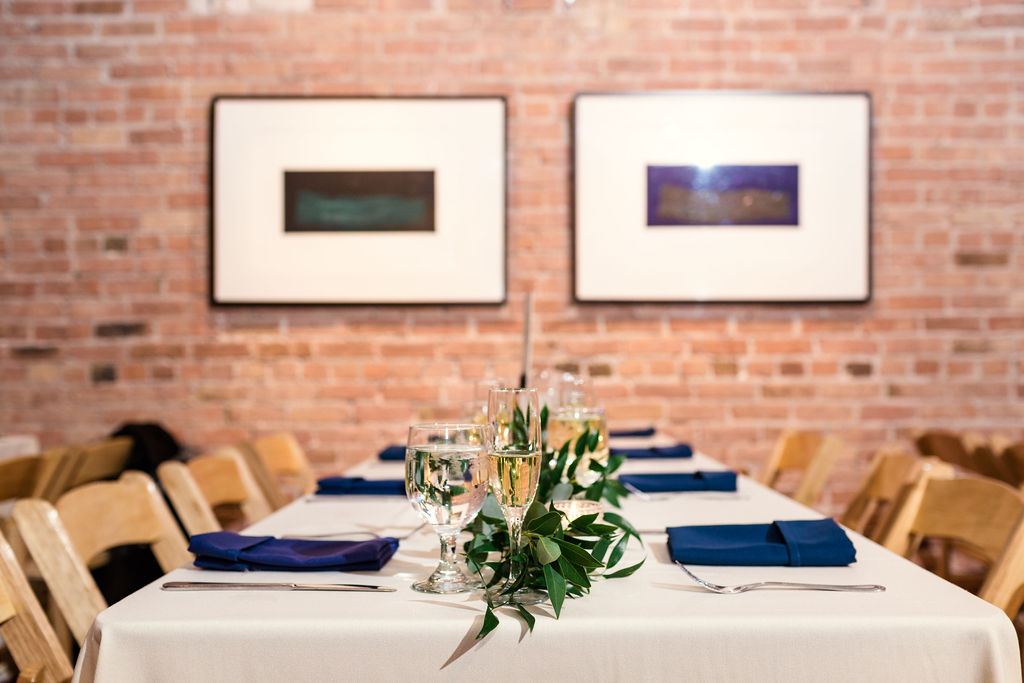 Simply elegant reception at Floating World Gallery with linens of white and blue and foliage garlands and votives lining the tables.