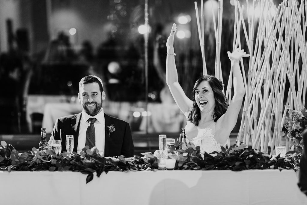 Bride and groom celebrating at the head table, lined with foliage and hand-poured votive candles for this all-greenery winter wedding in Chicago.