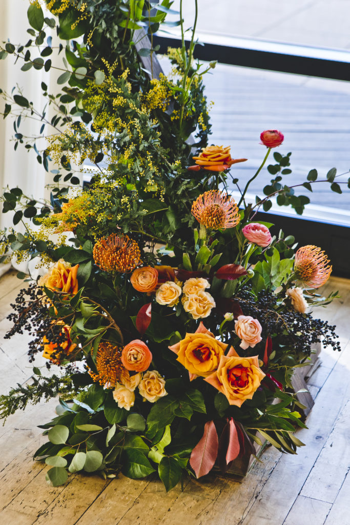 Contemporary wooden geometic ceremony alter bursting with colorful wildflower decorations and orange garden roses, pink ranunculus, and vivid protea. 