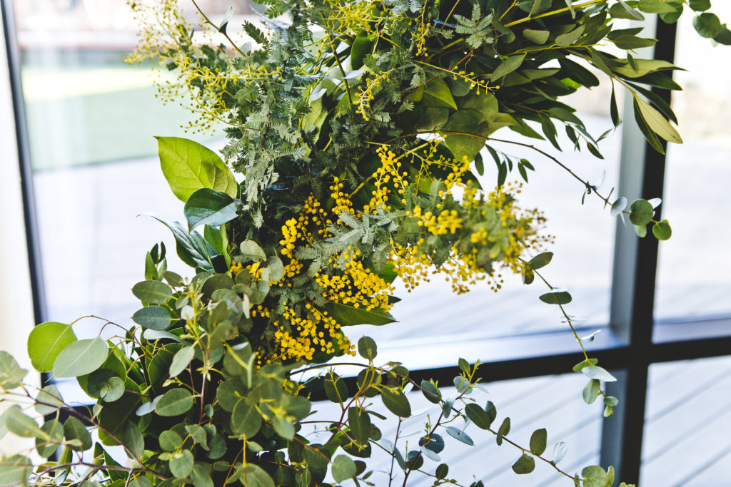 Yellow wildflowers and eucalyptus around a wooden, contemporary, geometric alter for a wedding ceremony at Greenhouse Loft.