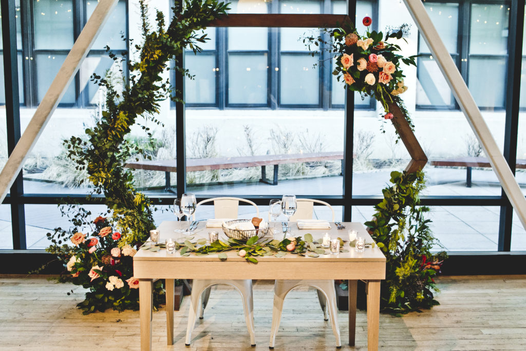 Sweetheart table and geometric wedding altar for playful reception with orange garden roses, pink ranunculus, and wildflowers.  Hexagonal wedding arch at Greenhouse Loft in Chicago.
