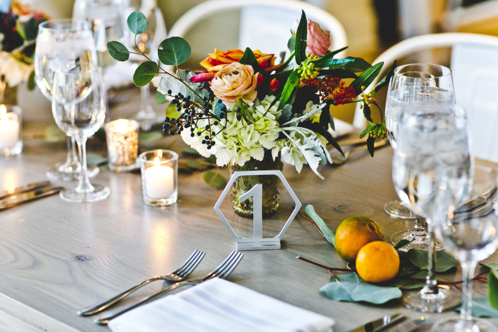 Greenhouse Loft colorful wedding reception details with coral ranunculus, orange garden roses, pale green hydrangea, hypericum berries, and dusty miller