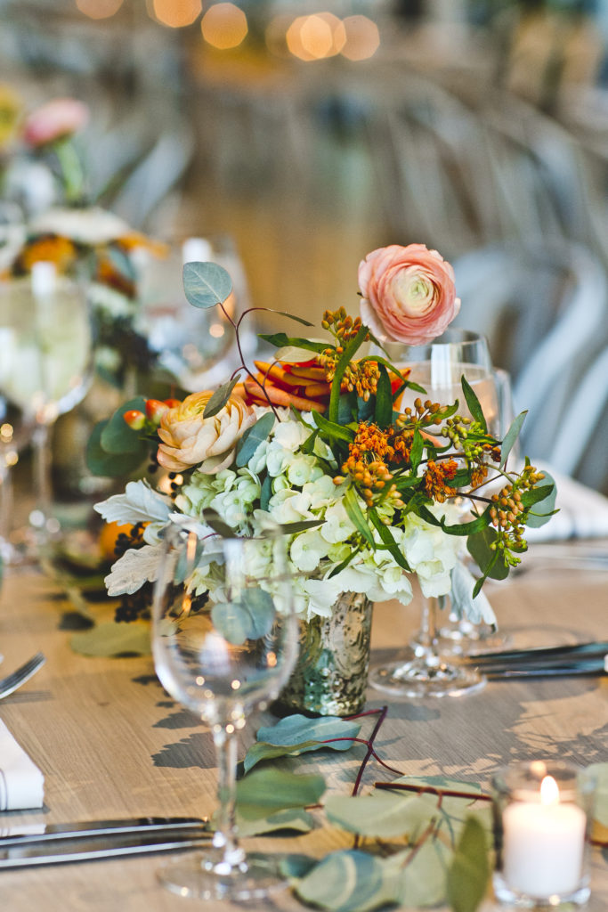 Greenhouse Loft colorful wedding reception details with coral ranunculus, orange garden roses, pale green hydrangea, hypericum berries, and dusty miller