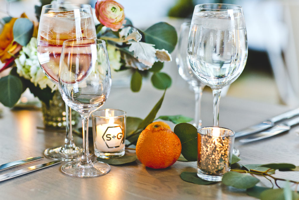 Wedding reception table details at Greenhouse Loft: playful accents like clementines, eucalyptus, small arrangements, votives, and metal table numbers.