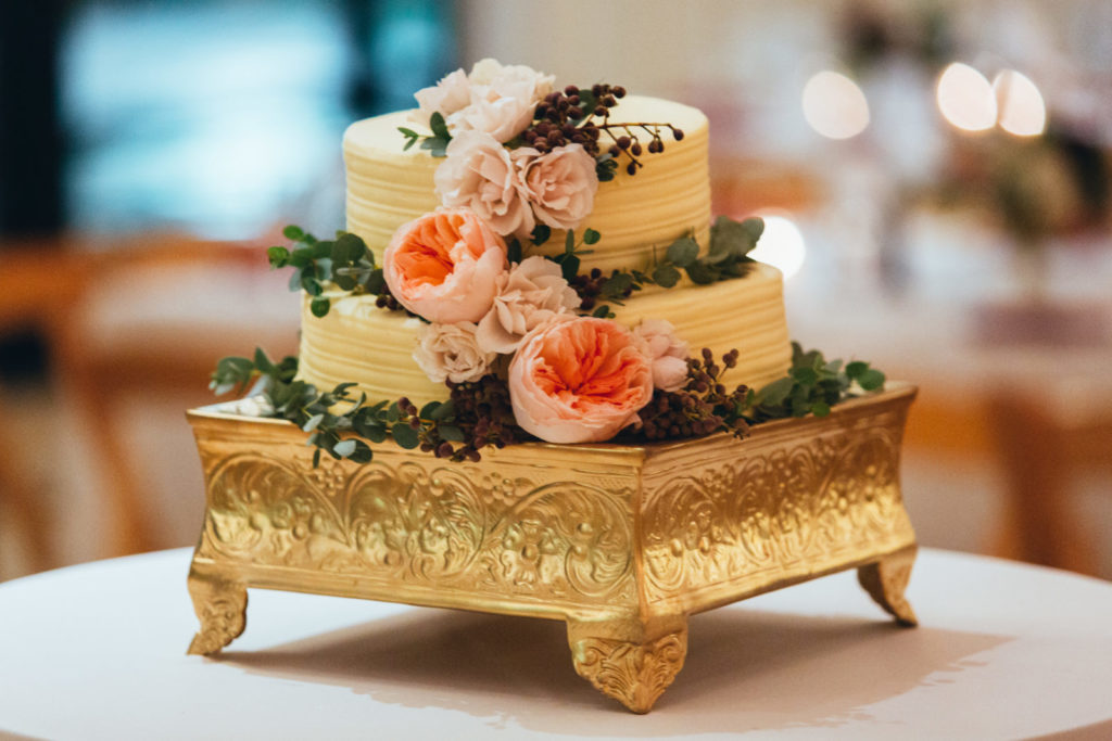 Romantic two-tiered vanilla wedding cake with cascading flowers in coral and dusty pink, on a gold gilded base for a wedding at Greenhouse Loft in Chicago.