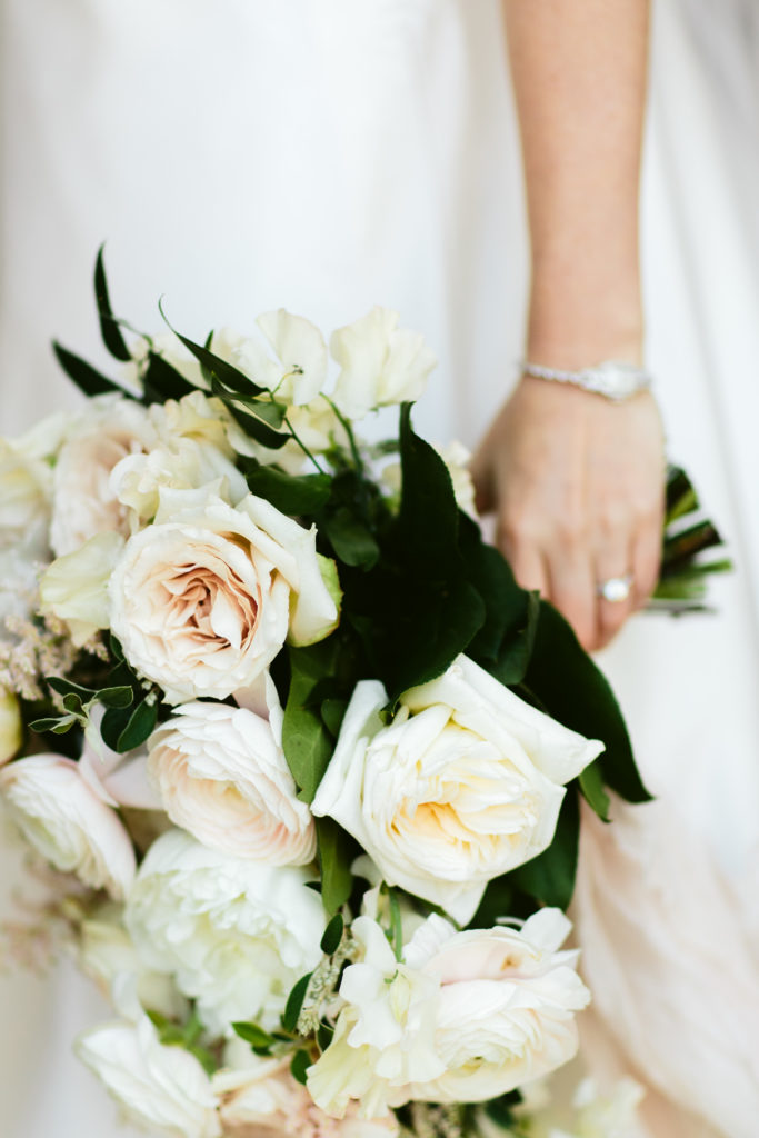 Bride holding a classic, beautiful bouquet with ivory peonies, blush ranunculus, garden roses, and sweet pea.