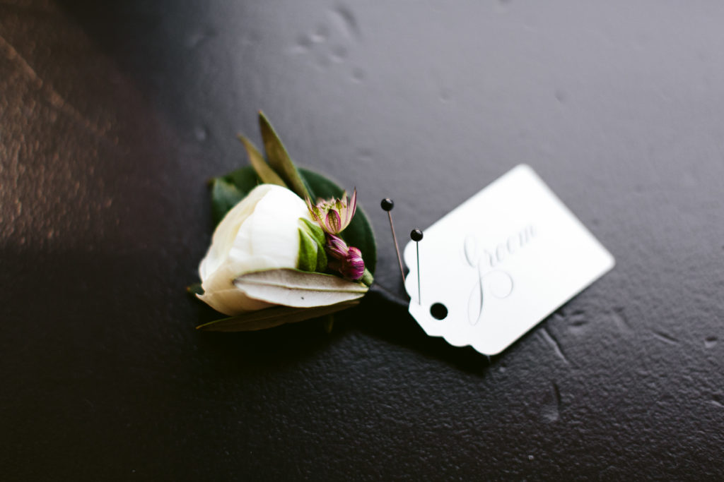 White ranunculus boutonnieres with tag for the groom.
