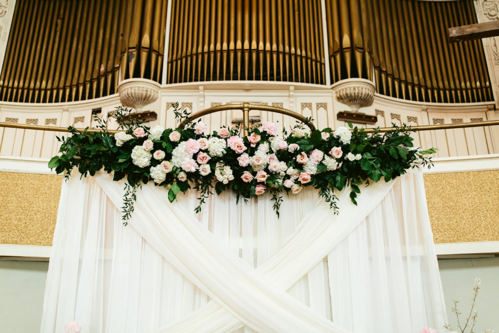 Opulent garden-style floral installation over a ceremonial backdrop for a spring wedding at Missio dei Wrigleyville in Chicago. Flowers include hydrangea, pink peonies, and garden roses.