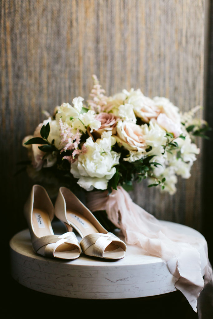 Bridal shoes with a classic bridal bouquet in ivory and blush with peonies, ranunculus, garden roses, and astilbe, tied with a blush sash.