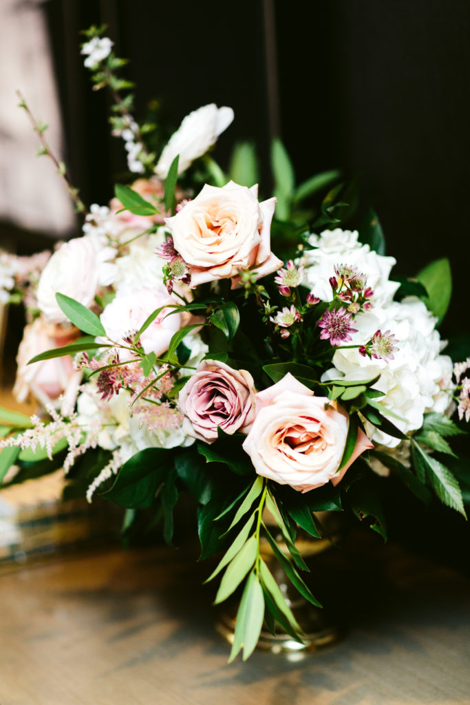 Garden roses in mauve and blush, ivory hydrangea, astilbe, and peonies for this spring wedding arrangement in a brass urn.  