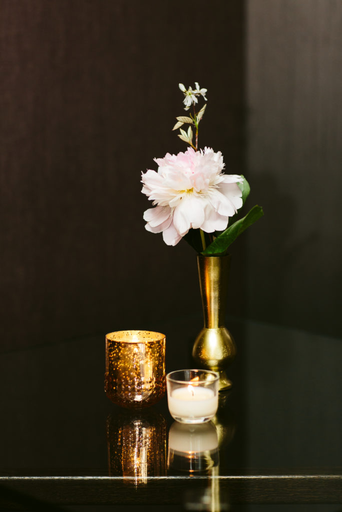 Blooming single peony in a single brass vase near two votives.