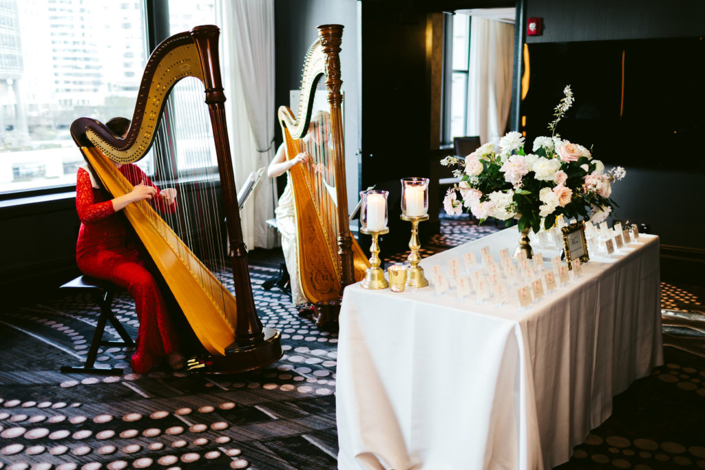 Harp players greeted guests behind this spring wedding escort card table, featuring a full arrangement of peonies, garden roses, flowering branches, and hydrangea.