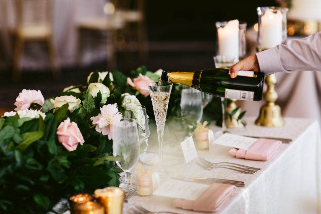 Pouring champagne for the couple's sweetheart table at their spring wedding, which featured lush pink peonies, garden roses, and white hydrangea.