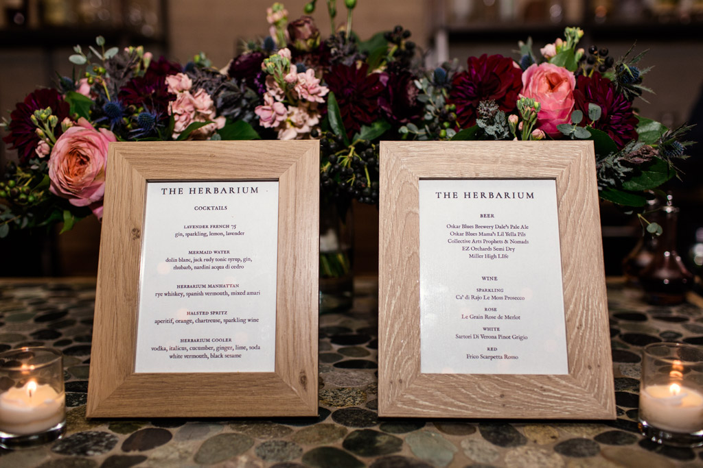 Herbarium drink menu's in front of the bridal parties bouquets of pink garden roses, blue thistle, plum scabiosa, eucalyptus, fern, maroon dahlias, and berries.