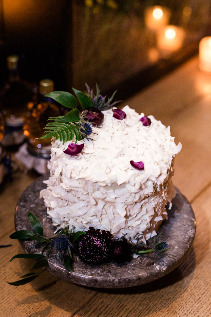 A coconut cake decorated with single petals, a blue thistle, and foliage for a rustic and romantic look at this vintage-inspired fall wedding in Chicago. 
