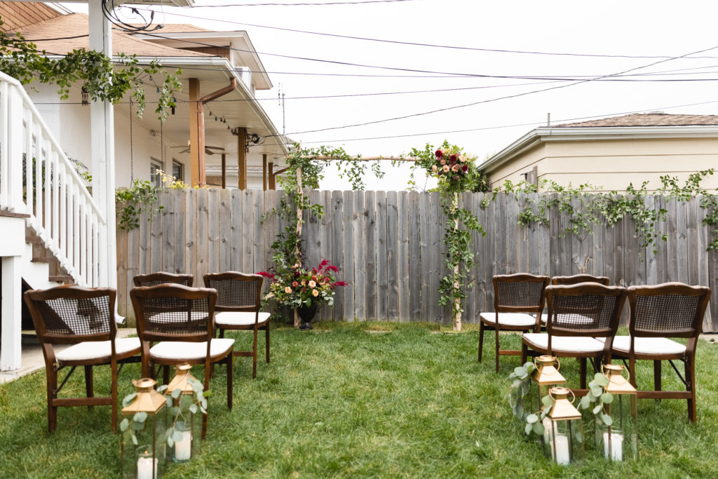 Micro backyard wedding with vintage cane chairs, a bird altar covered in foliage and flower accents, and brushed brass candle lanterns with eucalyptus.