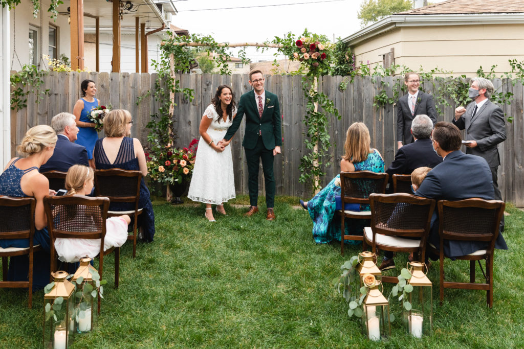 Micro backyard wedding with vintage cane chairs, a birch altar covered in foliage and flower accents, and brushed brass candle lanterns with eucalyptus.