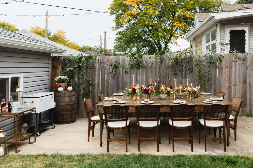 Warm wood tones, an autumn color palette, whisky bar, and small arrangements of blush and burgundy dahlias and pink zinnias for this early fall backyard wedding.