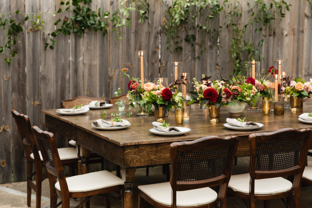 Warm wood tones, an autumn color palette, and small arrangements of blush and burgundy dahlias and pink zinnias for this early fall backyard wedding.